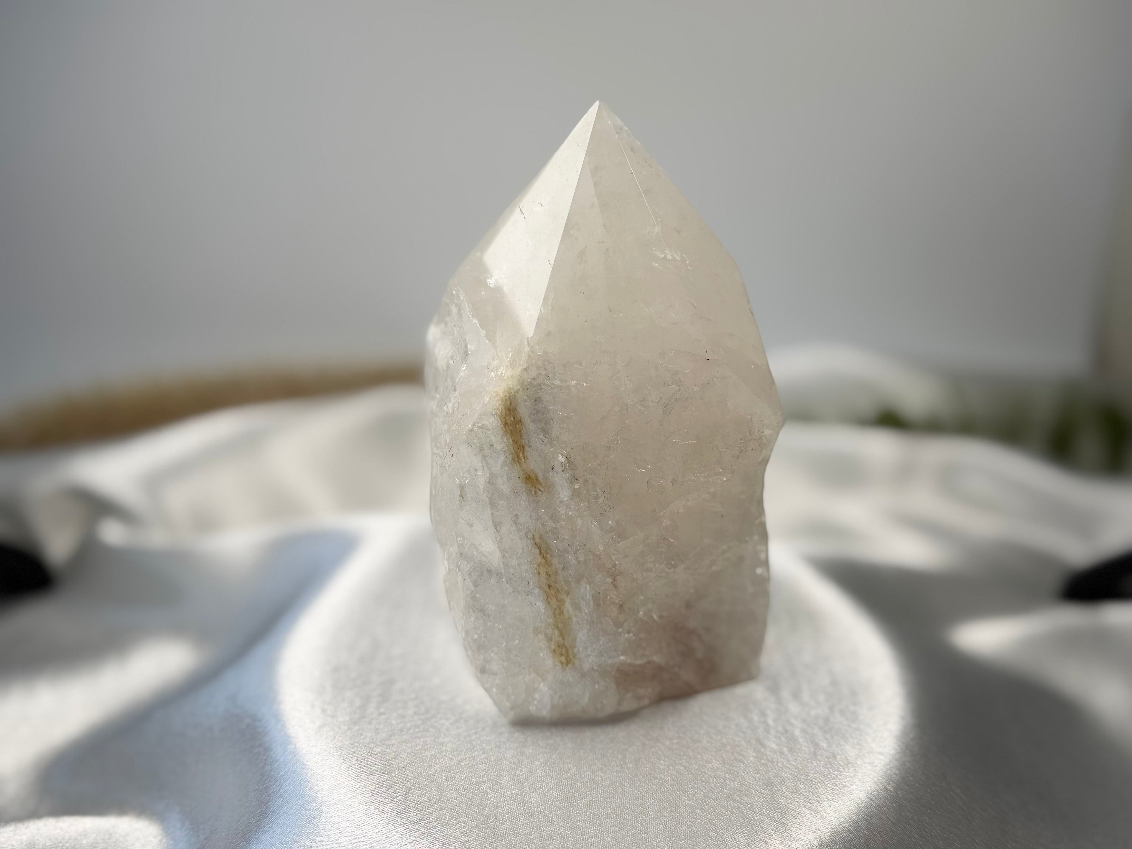 Treasured Energies clear quartz crystal tower with a polished point and raw natural base on white satin fabric