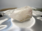 Treasured Energies clear quartz crystal point with a polished top and raw, natural base on a white satin background.