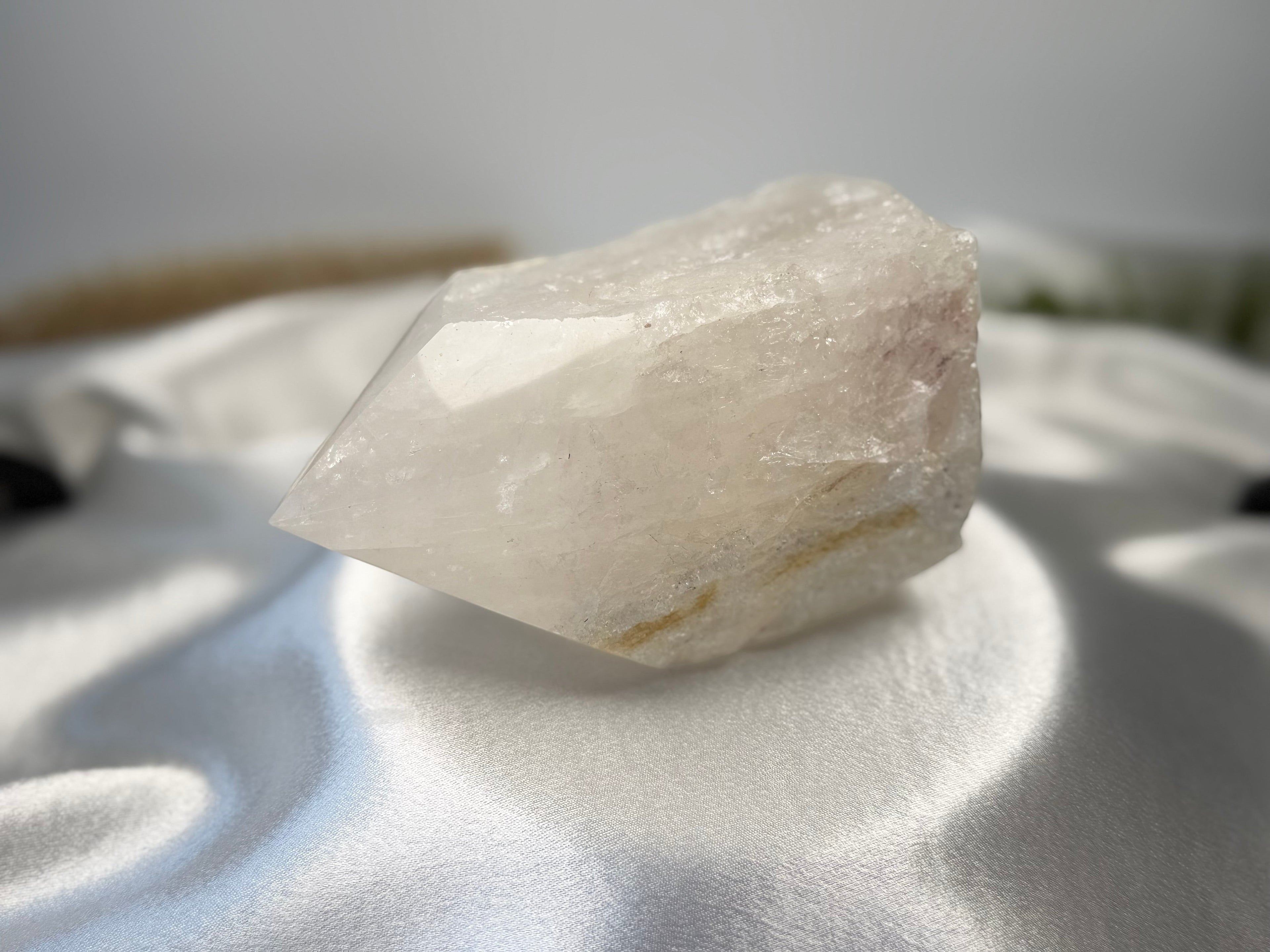 Treasured Energies clear quartz crystal point with a polished top and raw, natural base on a white satin background.