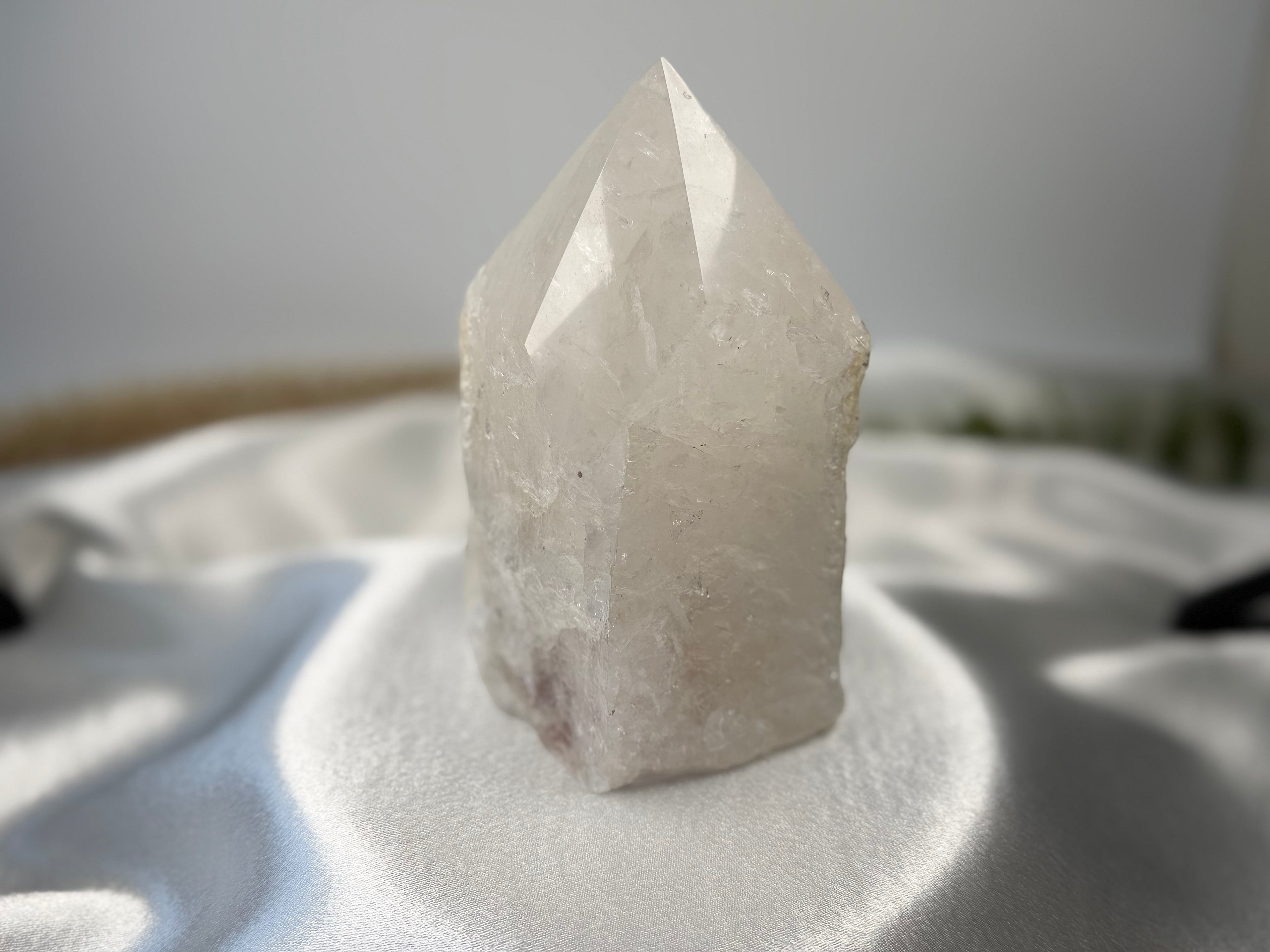 Treasured Energies clear quartz crystal tower with a polished point and raw, natural base on a white satin cloth.