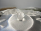 Treasured Energies clear quartz crystal sphere with visible phantom inclusions resting on a smooth white satin fabric.