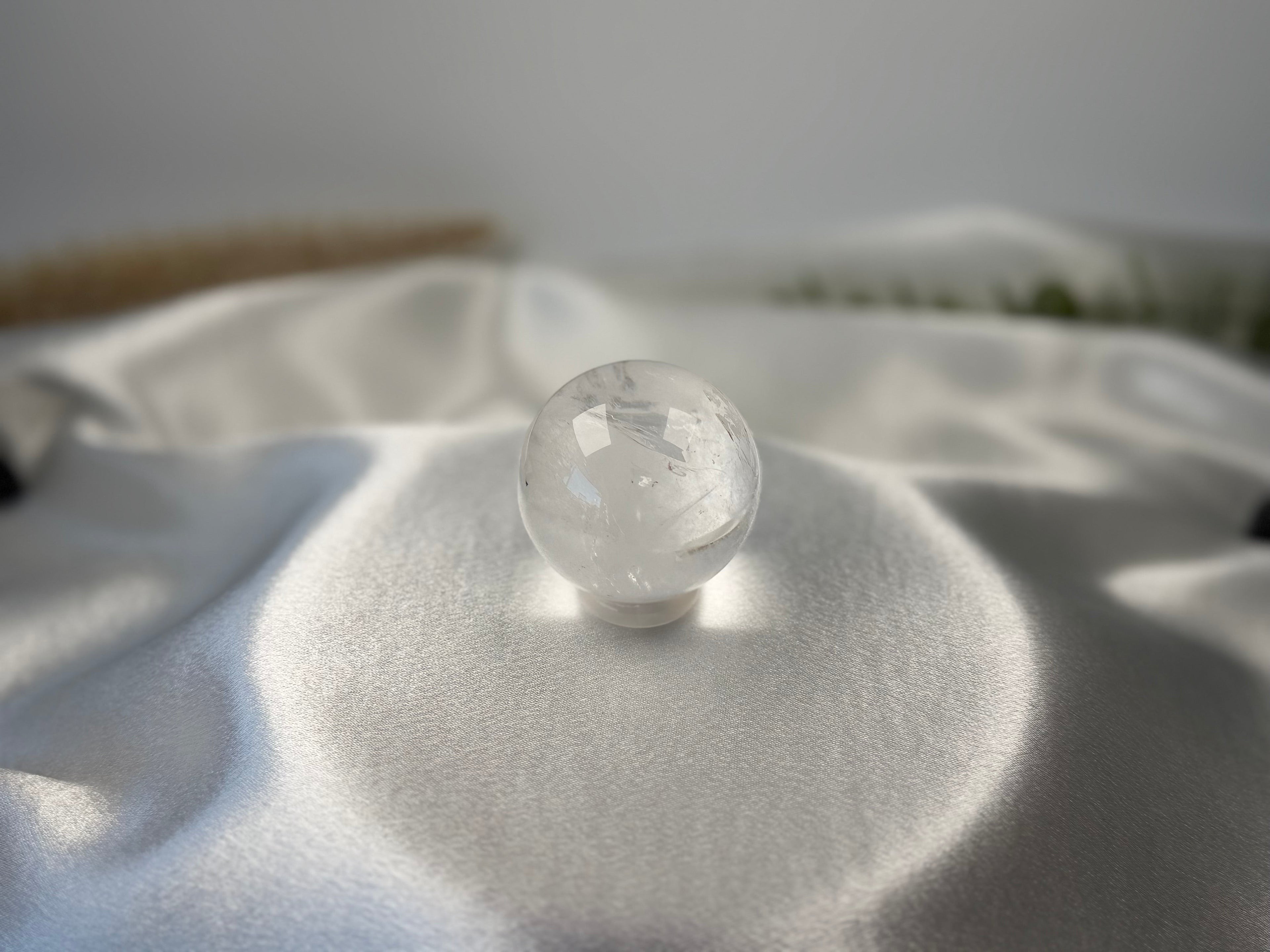 Treasured Energies clear quartz crystal sphere with visible phantom inclusions resting on a smooth white satin fabric.