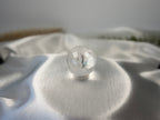 Treasured Energies clear quartz crystal sphere with internal phantom inclusions resting on white satin fabric.