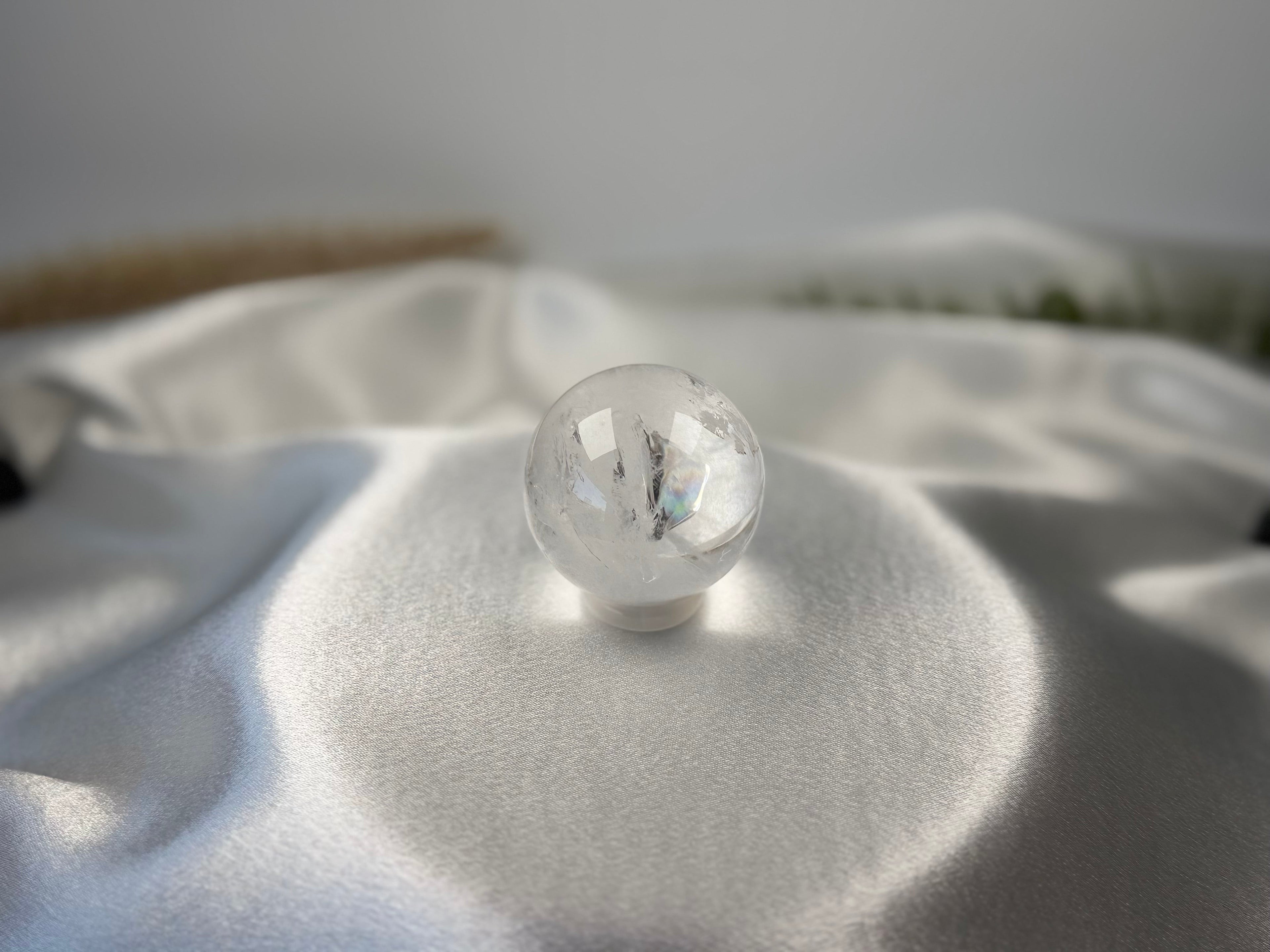 Treasured Energies clear quartz crystal sphere with internal phantom inclusions resting on white satin fabric.