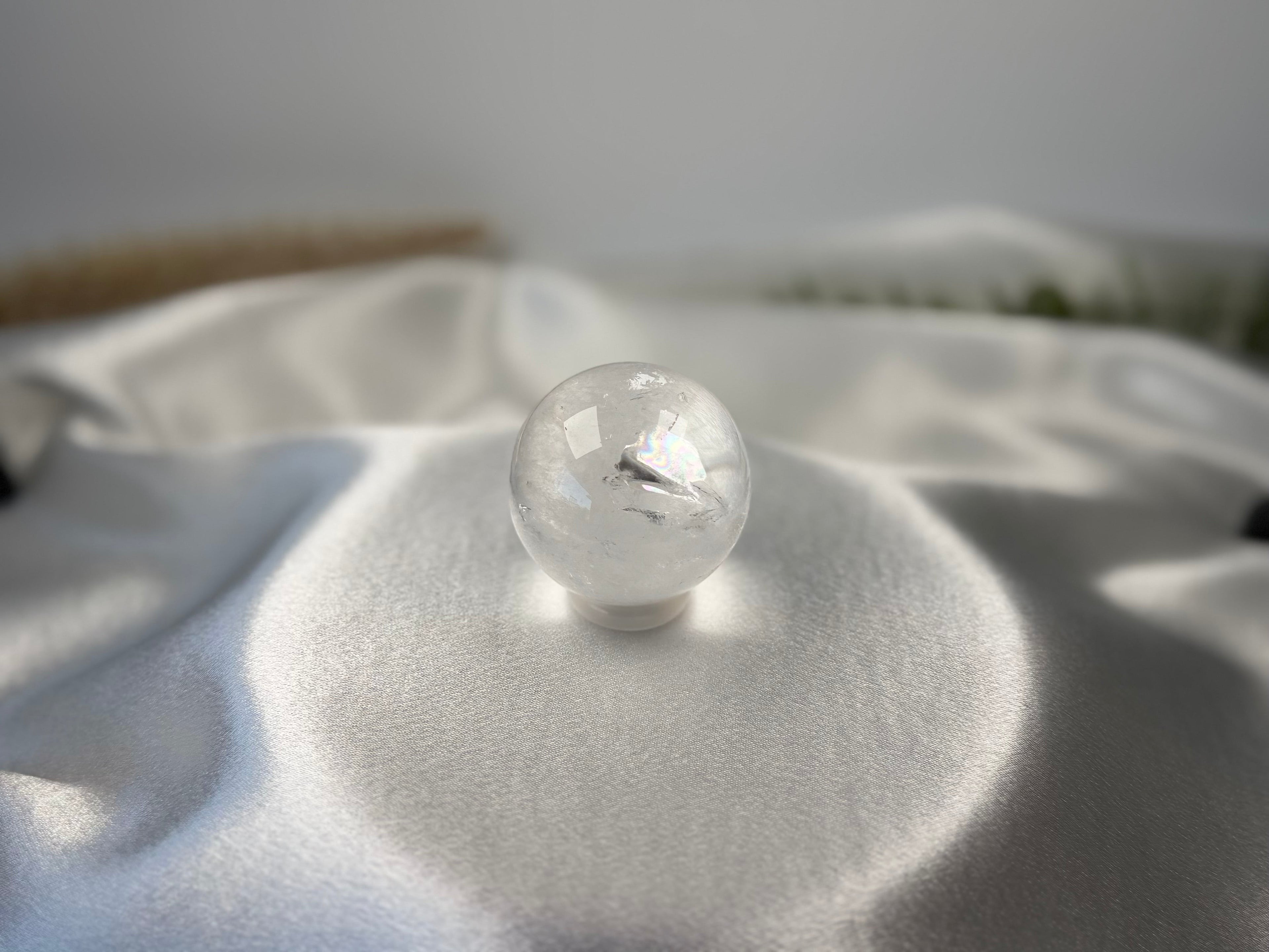 Treasured Energies clear quartz crystal sphere with visible phantom inclusions resting on a white satin fabric background