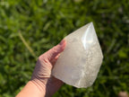 Treasured Energies clear quartz crystal tower with a polished point and raw base held in a hand outdoors