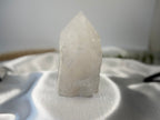 Treasured Energies clear quartz crystal tower with a raw base and polished point on a white satin background.