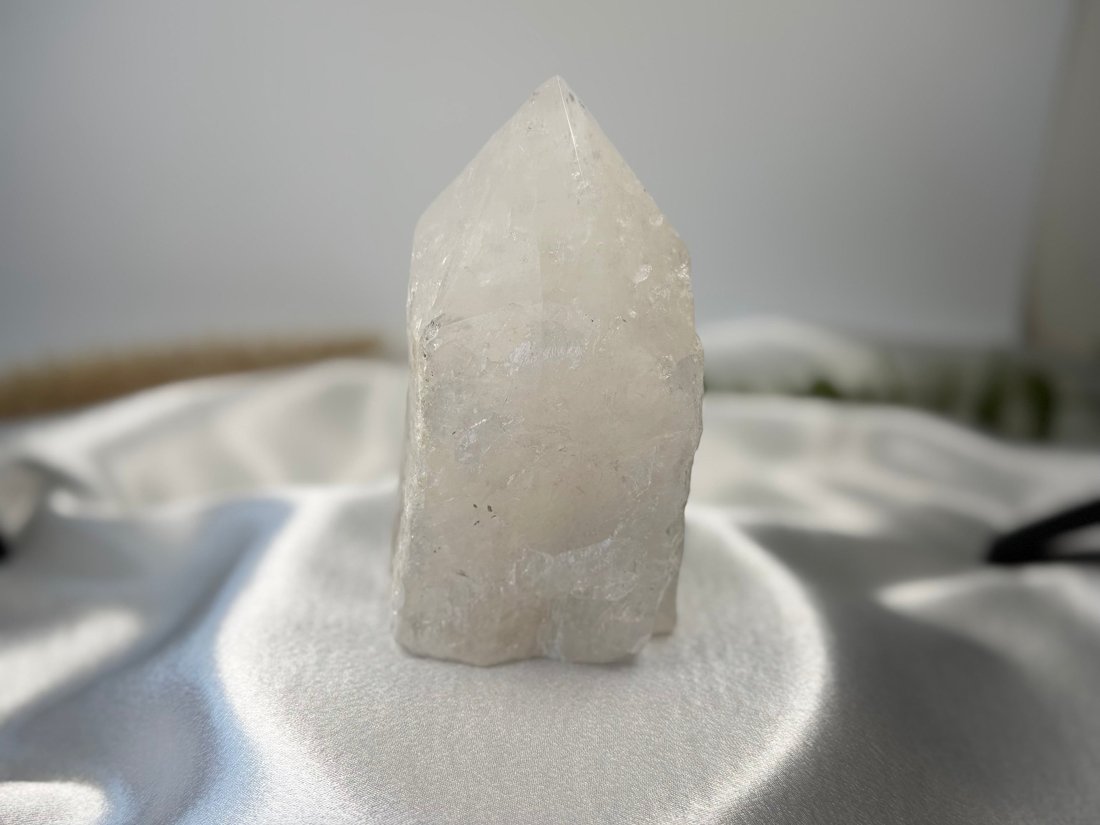 Treasured Energies clear quartz crystal tower with a raw base and polished point on a white satin background.