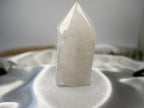 Treasured Energies clear quartz crystal tower with a polished point and raw natural base on white satin fabric