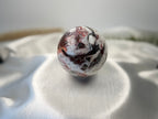 Treasured Energies polished Crazy Lace Agate crystal sphere with intricate red, white, and grey swirling patterns.