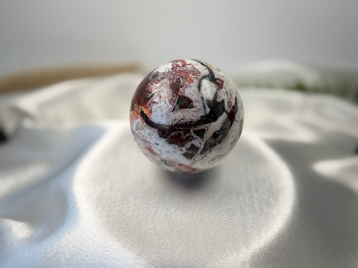 Treasured Energies polished Crazy Lace Agate crystal sphere with intricate red, white, and grey swirling patterns.