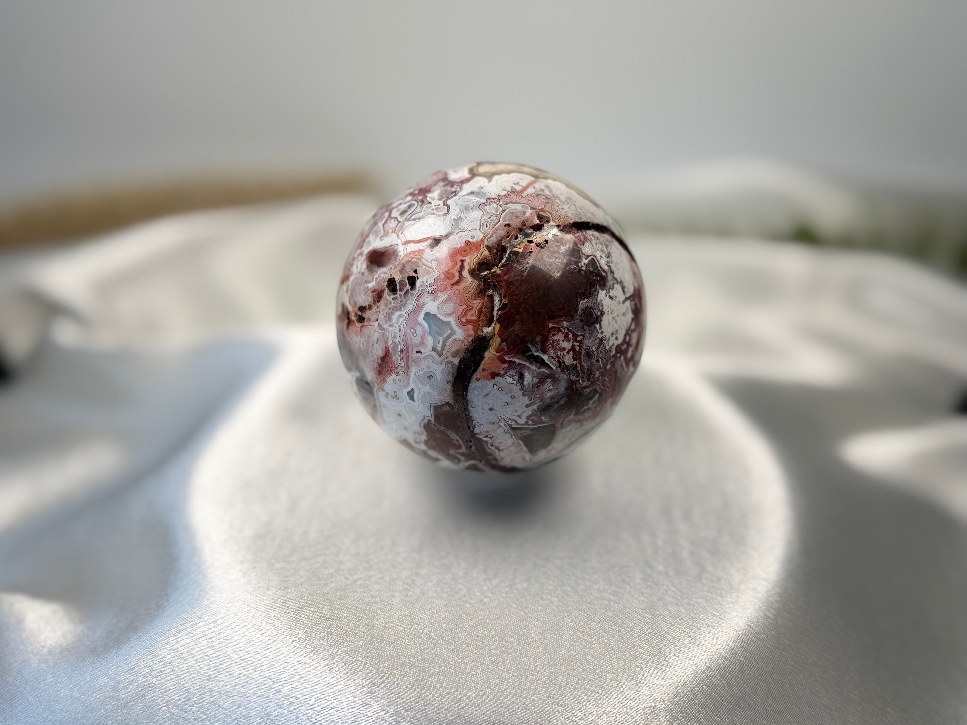 Treasured Energies polished Crazy Lace Agate crystal sphere with intricate red, white, and grey swirling patterns.