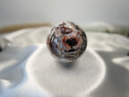 Treasured Energies polished Crazy Lace Agate crystal sphere with intricate red, white, and grey swirling patterns.