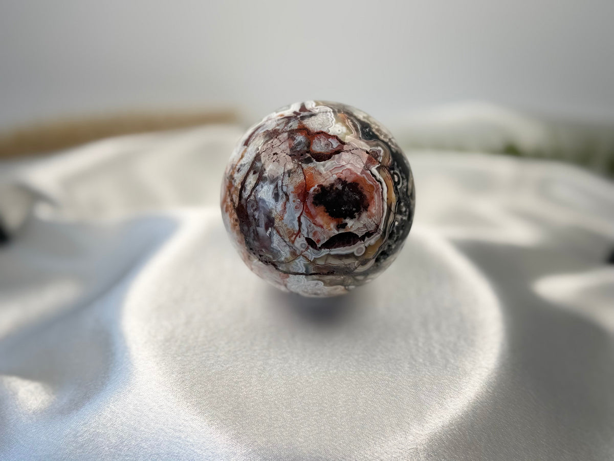 Treasured Energies polished Crazy Lace Agate crystal sphere with intricate red, white, and grey swirling patterns.