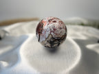 Treasured Energies polished Crazy Lace Agate crystal sphere with intricate red, white, and brown swirling patterns.