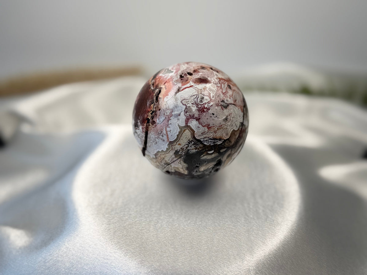 Treasured Energies polished Crazy Lace Agate crystal sphere with intricate red, white, and brown swirling patterns.