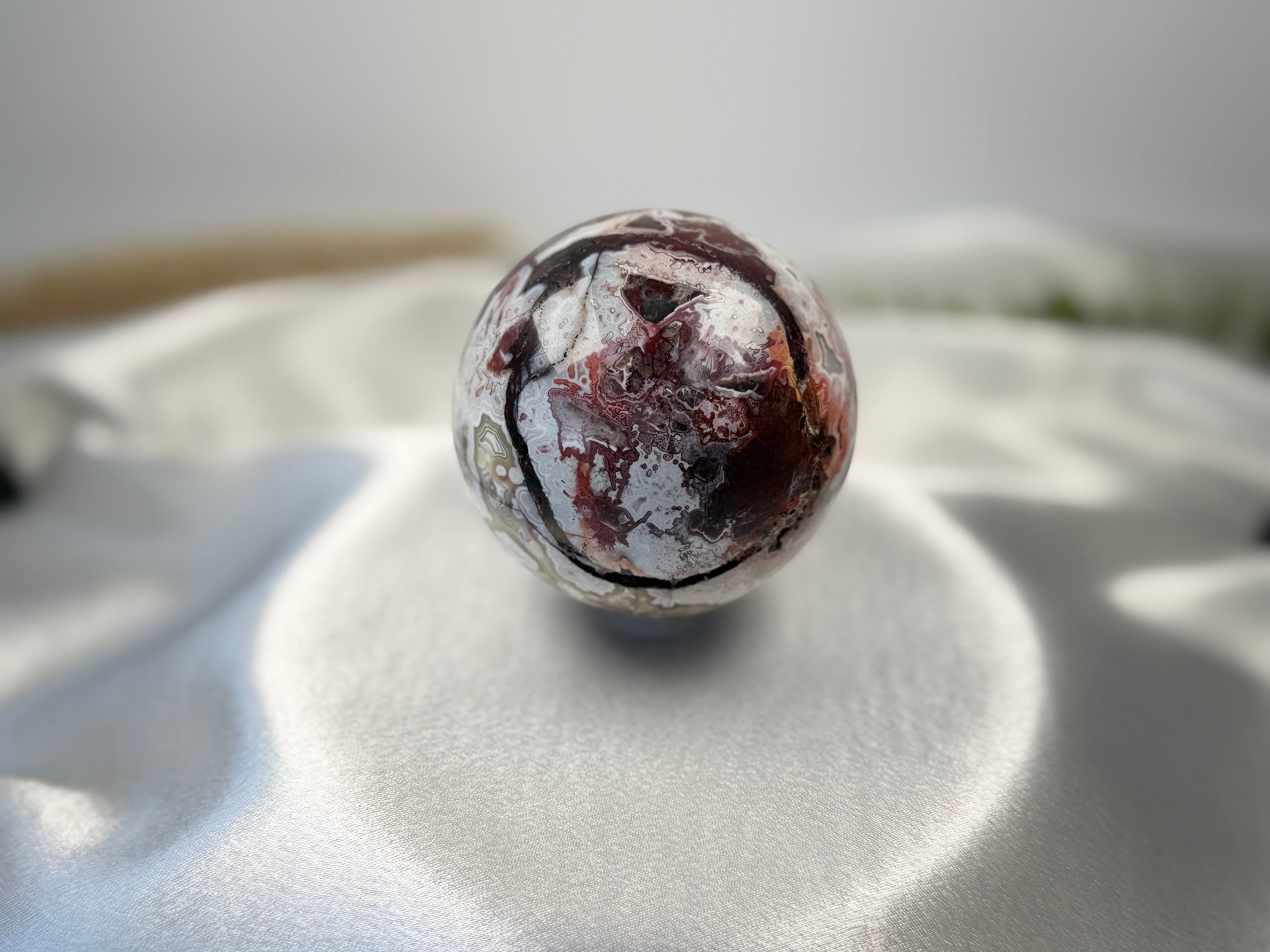 Treasured Energies polished Crazy Lace Agate crystal sphere with intricate red, white, and grey swirling patterns.