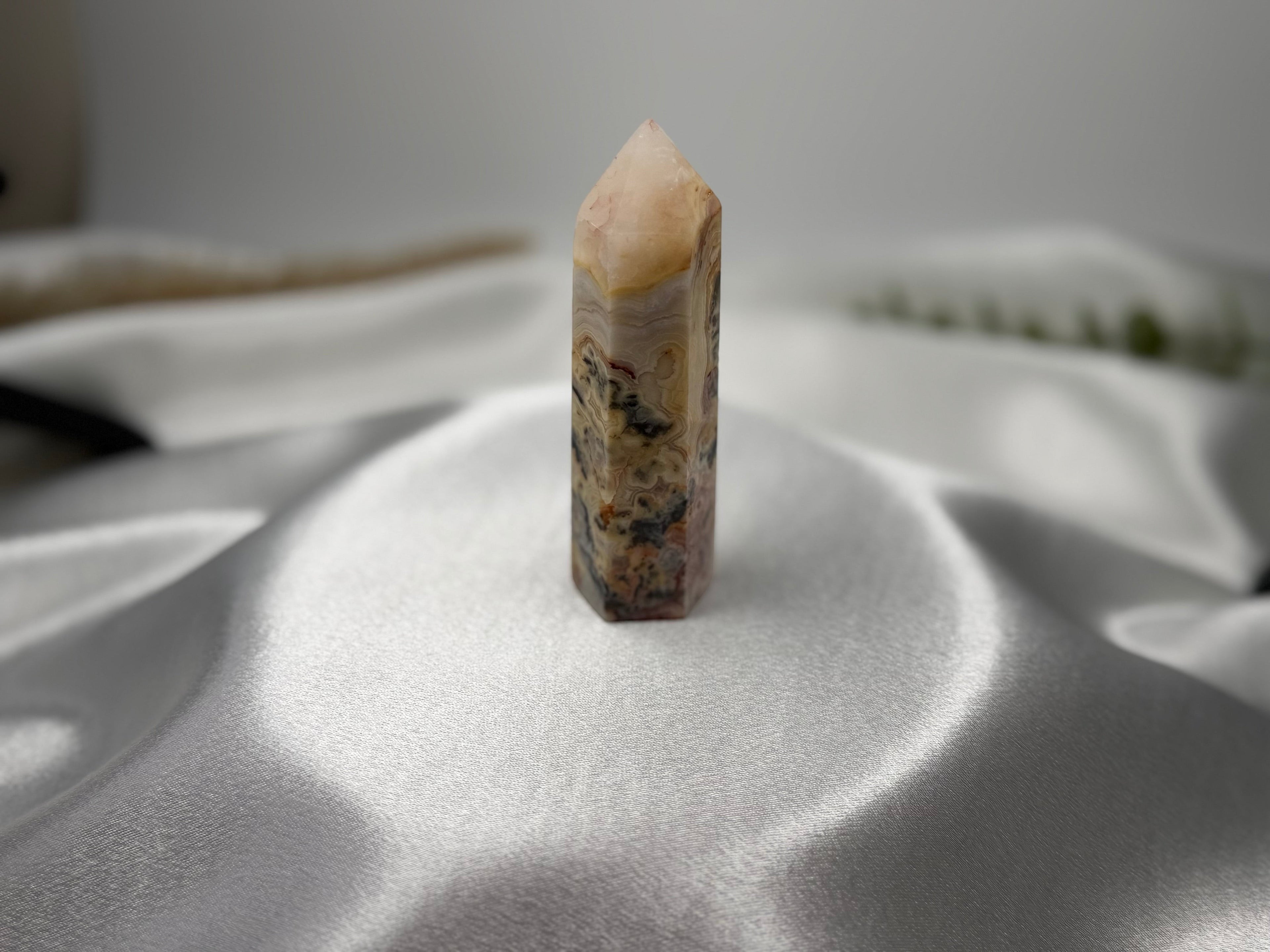 Treasured Energies Crazy Lace Agate crystal tower with intricate swirling patterns on a white satin background.