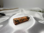 Treasured Energies Crazy Lace Agate crystal tower with orange, cream, and grey swirling patterns on white satin.