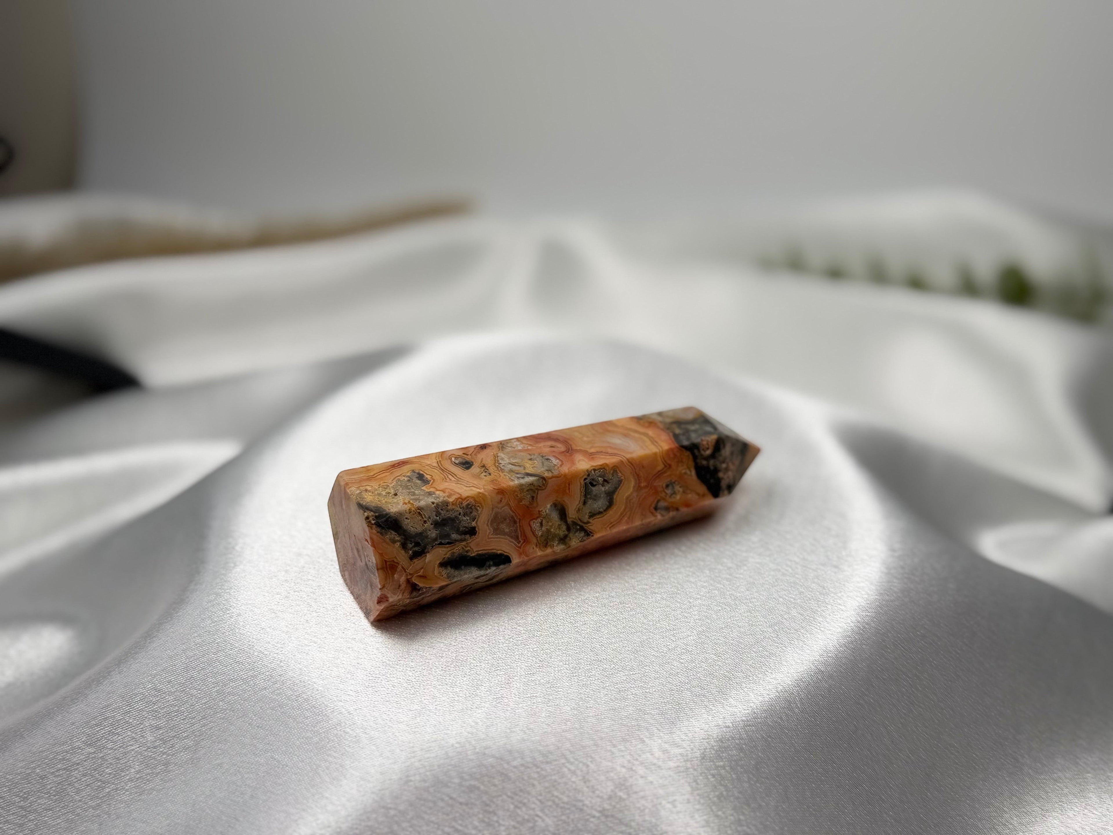 Treasured Energies Crazy Lace Agate crystal tower with orange, cream, and grey swirling patterns on white satin.