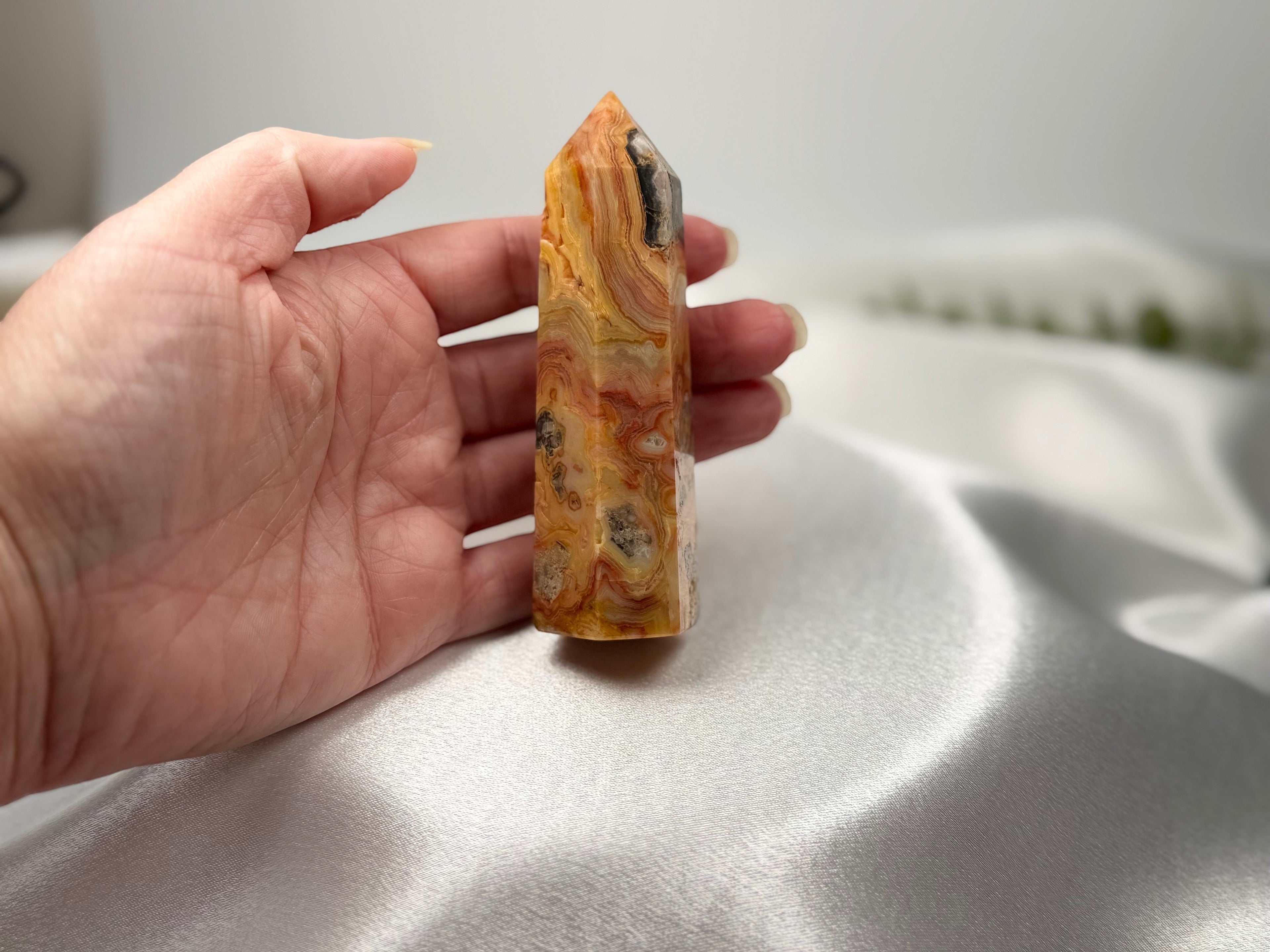 Treasured Energies Crazy Lace Agate crystal tower held in a hand against a white satin background