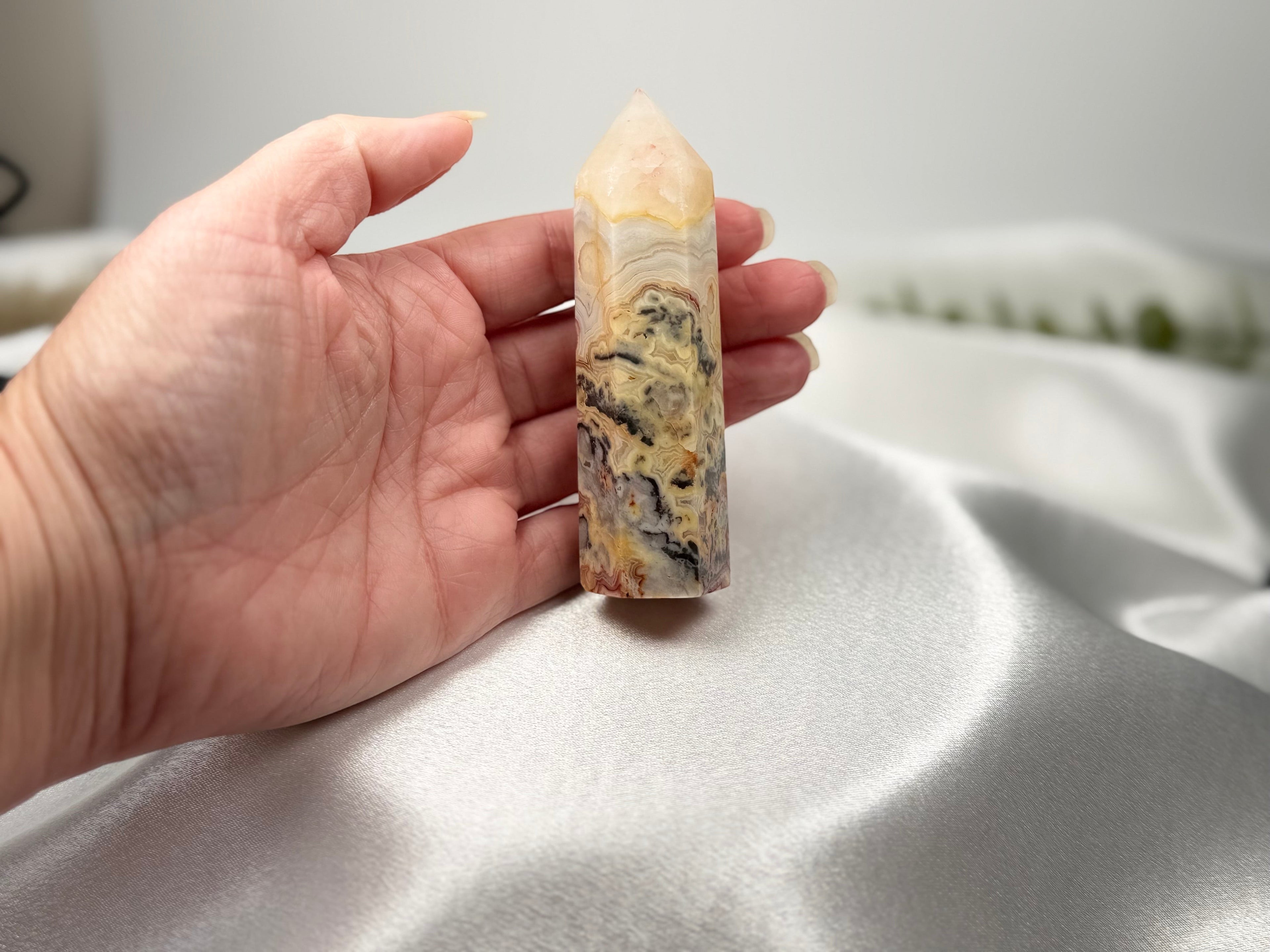 Treasured Energies Crazy Lace Agate crystal tower held in a hand, showing intricate cream and brown swirling patterns.