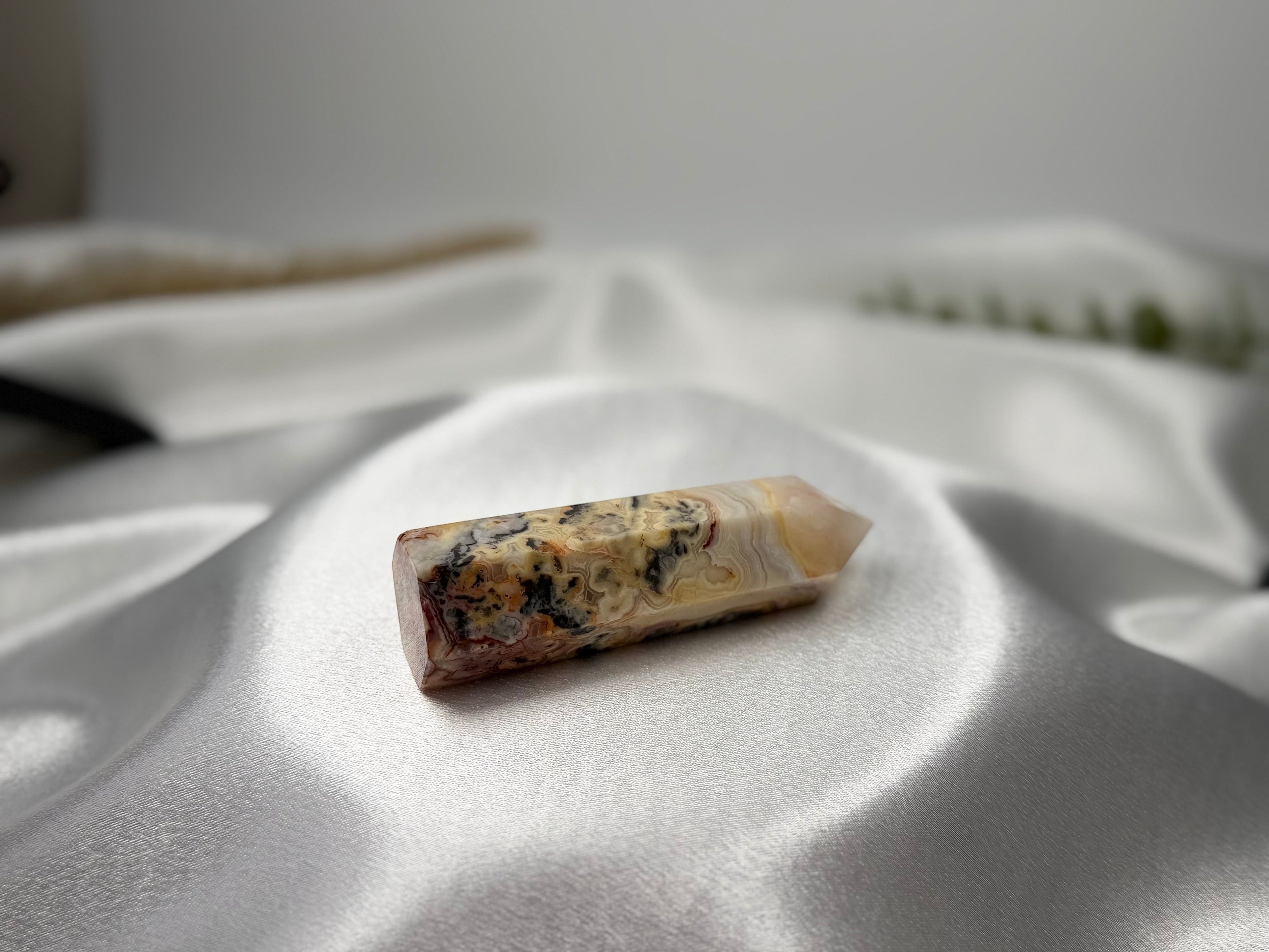 Treasured Energies Crazy Lace Agate crystal tower with intricate swirling patterns on a white satin fabric background.