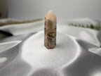 Treasured Energies Crazy Lace Agate crystal tower with intricate swirling patterns in cream, red, and grey on satin.