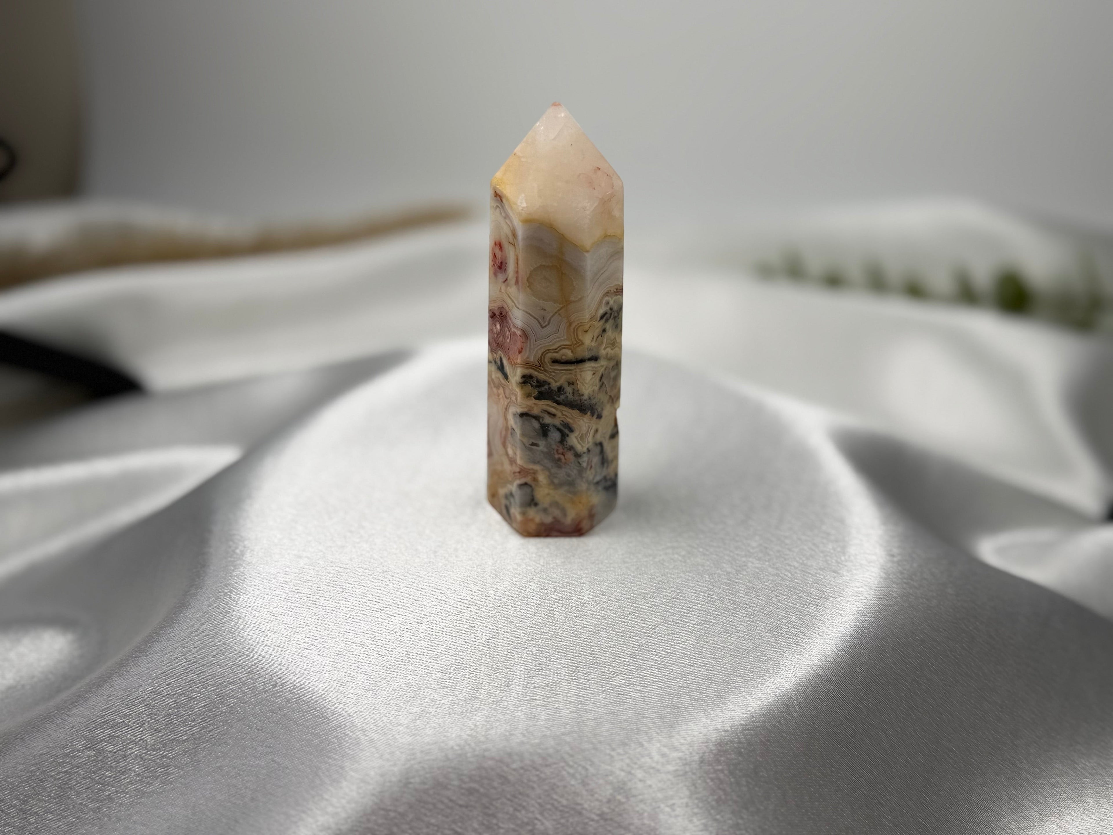 Treasured Energies Crazy Lace Agate crystal tower with intricate swirling patterns in cream, red, and grey on satin.