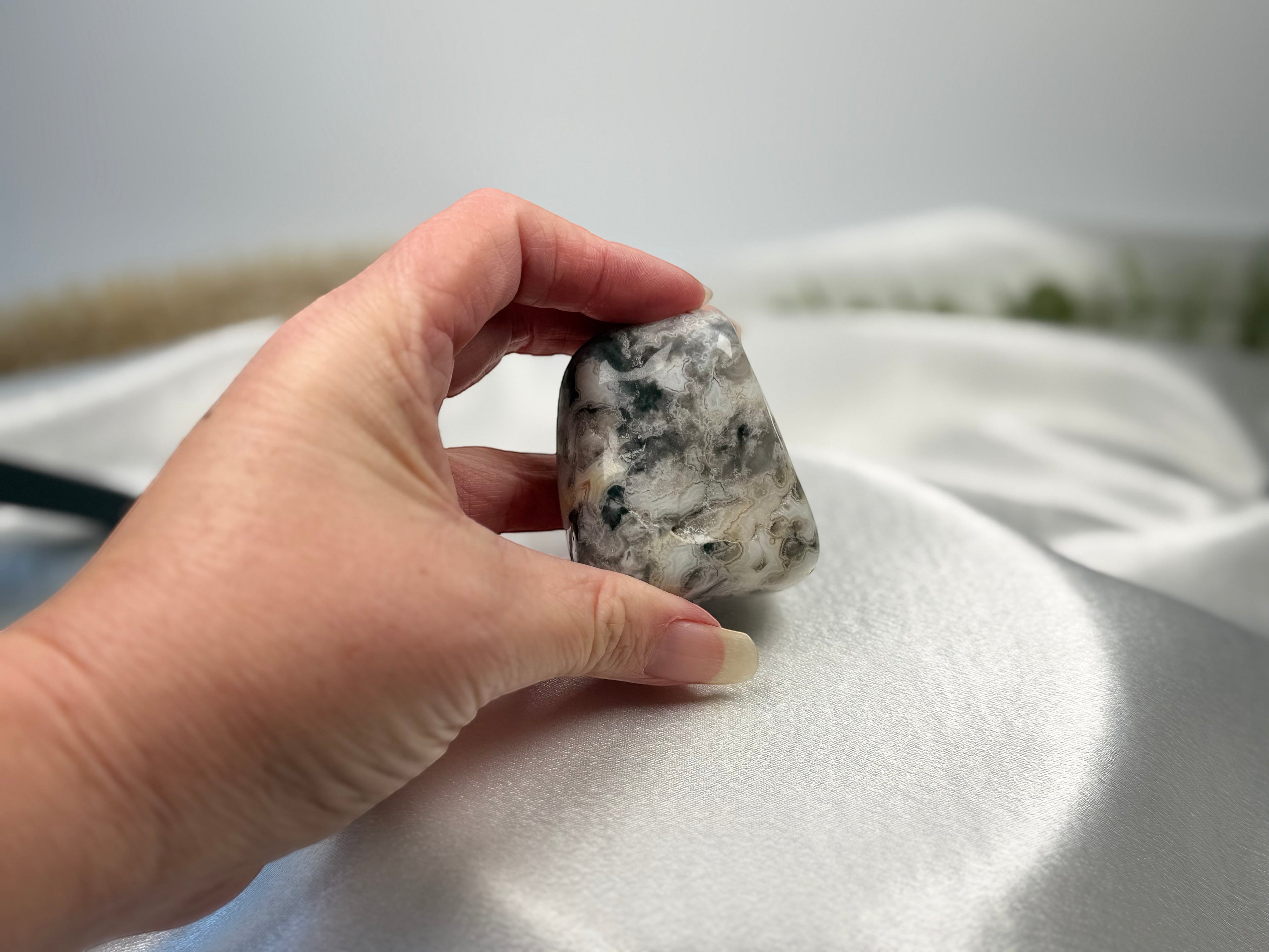 Treasured Energies tumbled Crazy Lace Agate crystal held in a hand, showing intricate grey and white swirling patterns.