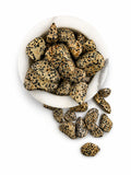 Treasured Energies tumbled Dalmatian Jasper stones with black spots in a white marble bowl on a white background.