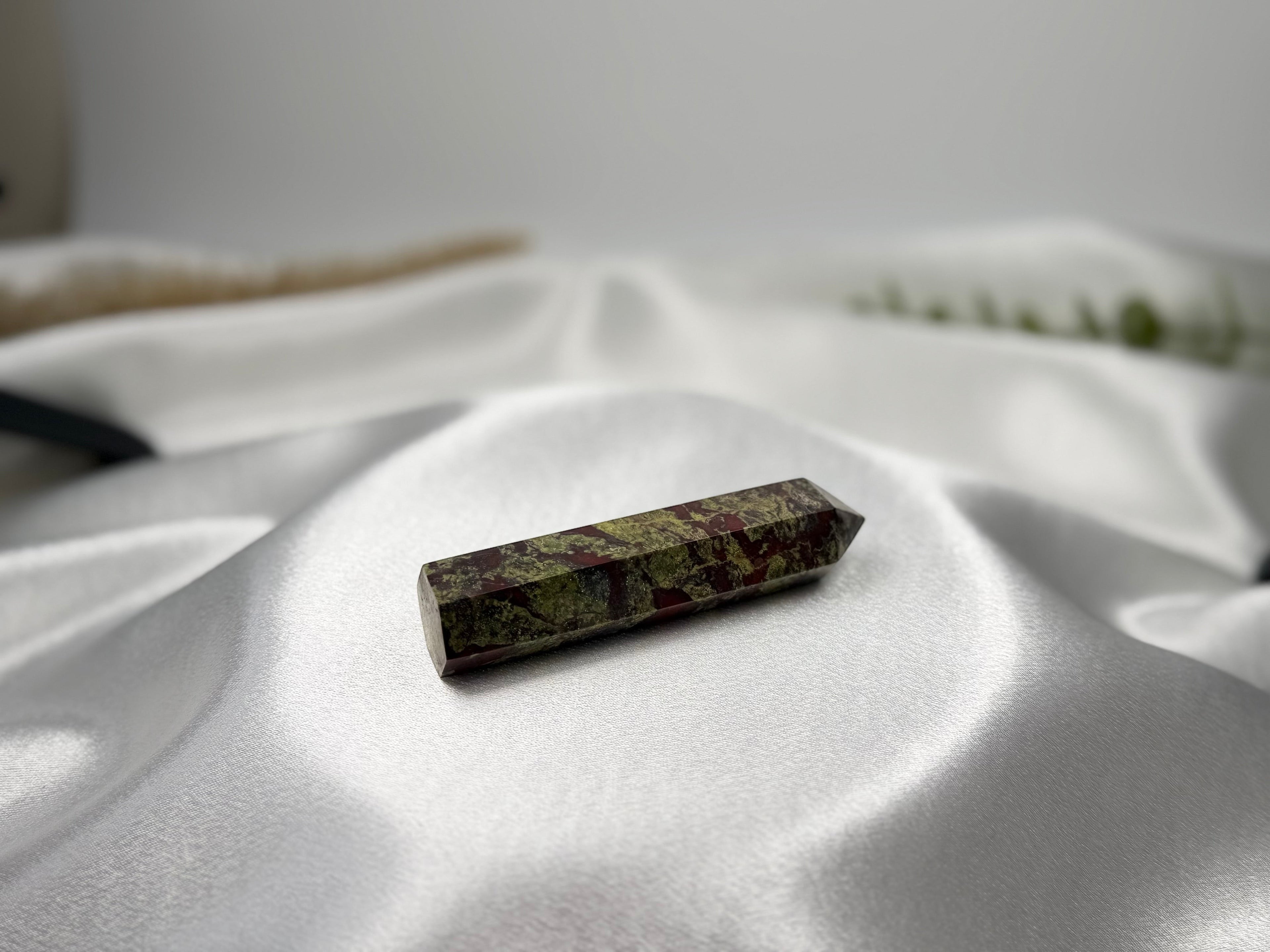 Treasured Energies Dragon Blood Jasper crystal tower with green and red patterns on a soft white satin background.