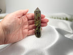 Treasured Energies Dragon Blood Jasper crystal tower held in hand against a white satin background.