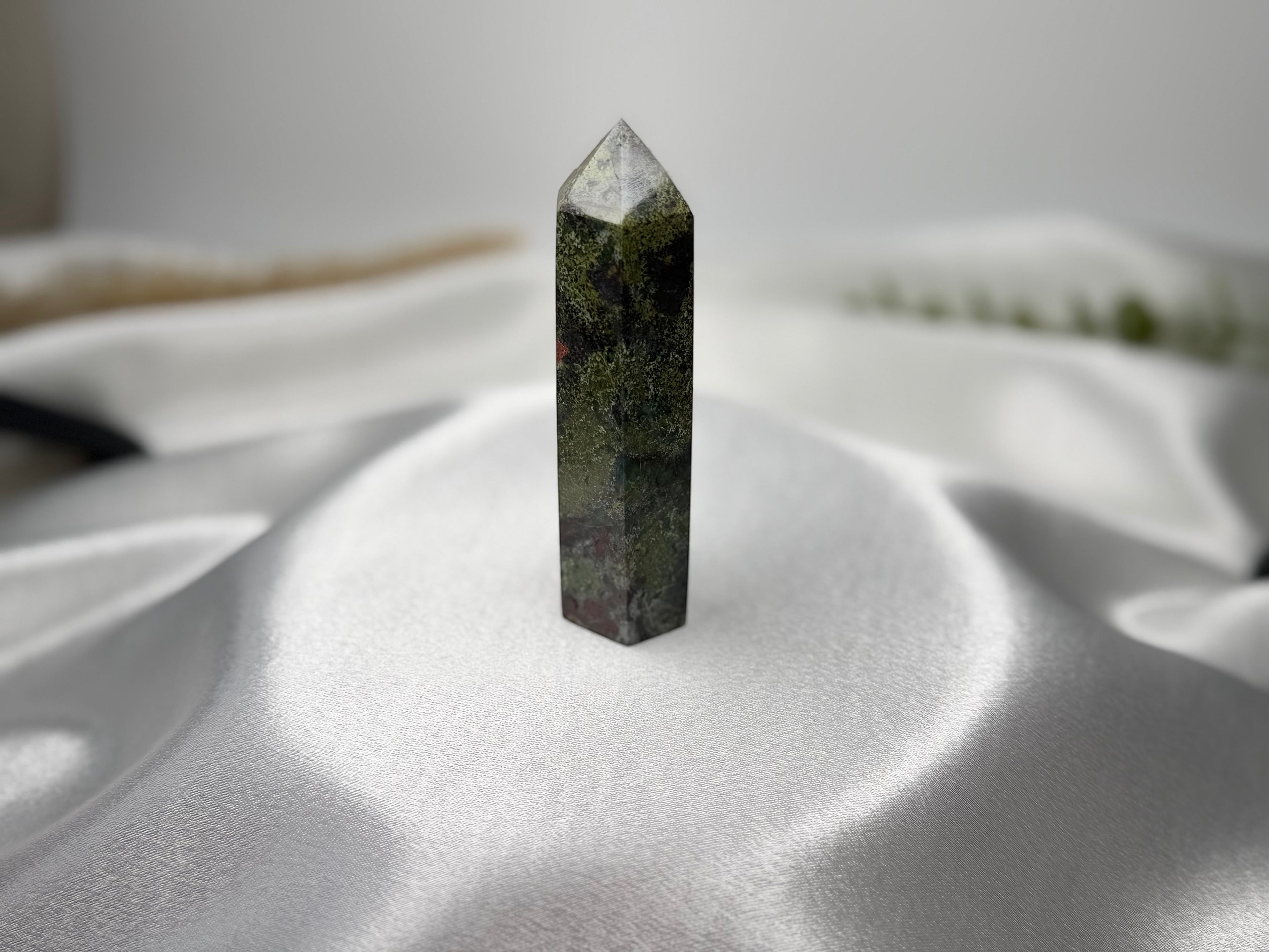 Treasured Energies Dragon Blood Jasper crystal tower with green and red patterns on a white satin background.
