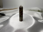 Treasured Energies Dragons Blood Jasper crystal tower with green and red patterns on a white satin background.