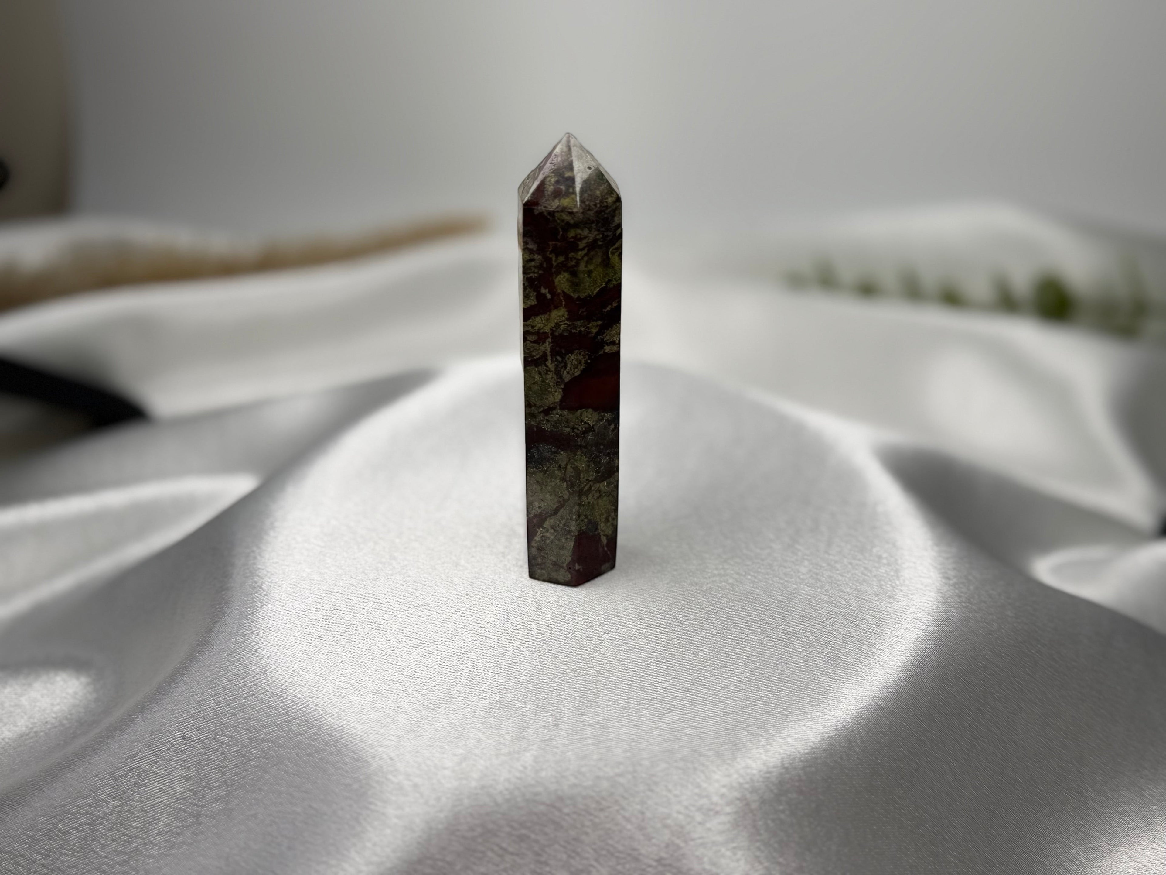 Treasured Energies Dragons Blood Jasper crystal tower with green and red patterns on a white satin background.