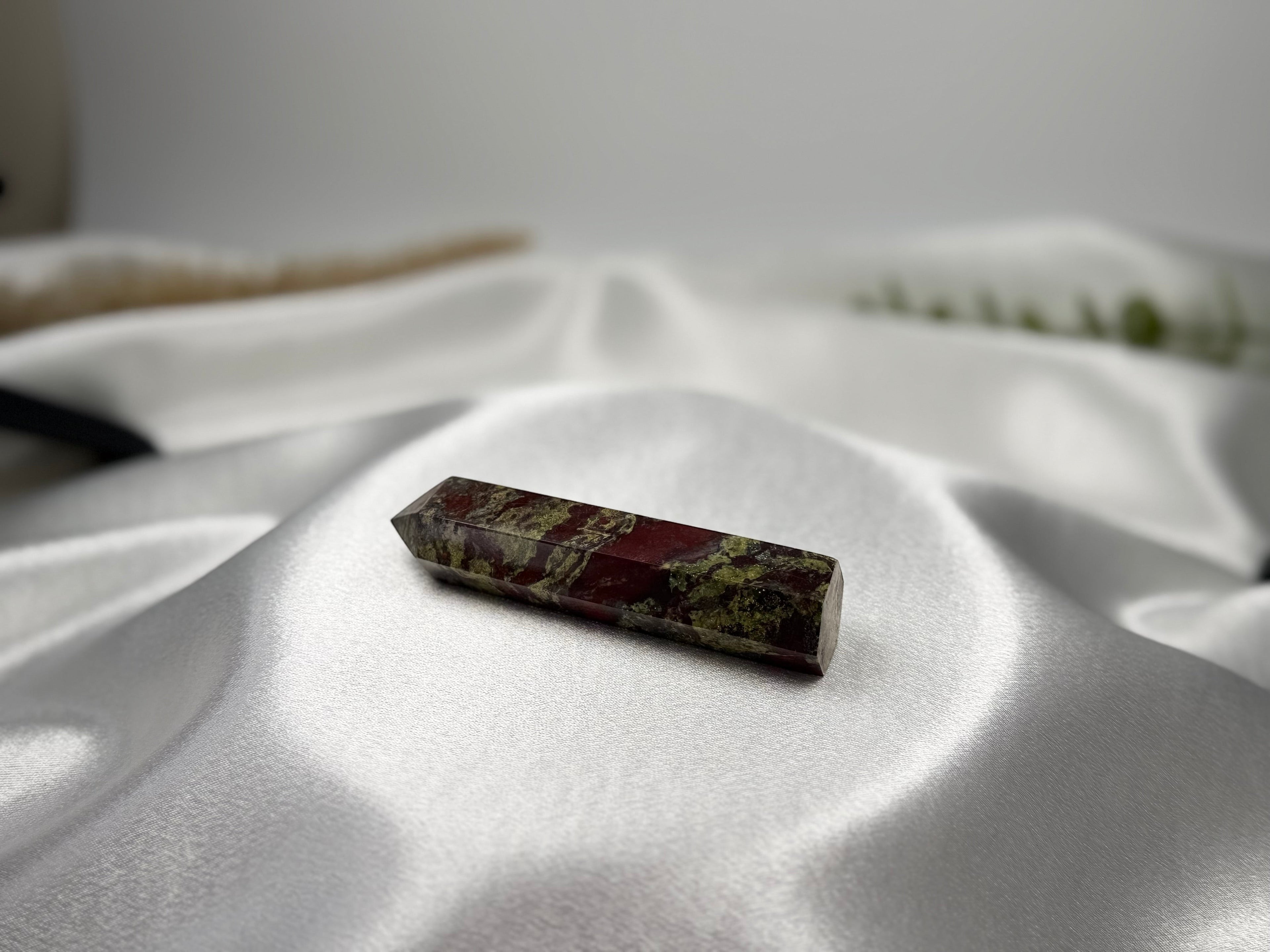 Treasured Energies Dragons Blood Jasper crystal tower with red and green patterns on a white satin background