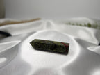 Treasured Energies Dragons Blood Jasper crystal tower with green and red patterns resting on white satin fabric.
