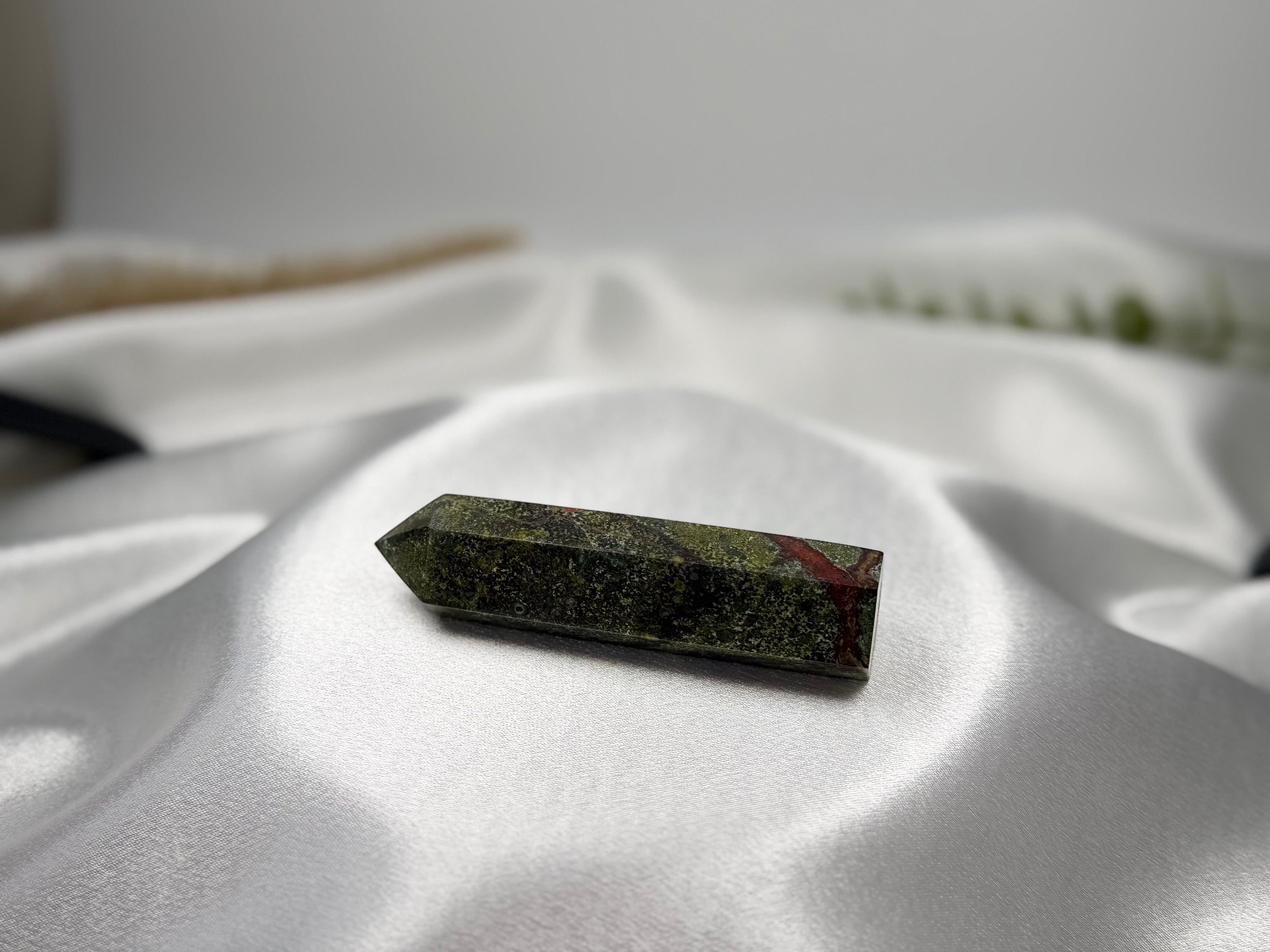Treasured Energies Dragons Blood Jasper crystal tower with green and red patterns resting on white satin fabric.