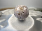 Treasured Energies flower agate crystal sphere with druzy inclusions resting on a white satin fabric background.
