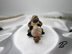 Treasured Energies flower agate crystal heart held by a small platypus figurine on a white satin background