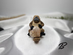 Treasured Energies flower agate crystal heart held by a small platypus figurine on a white satin background.