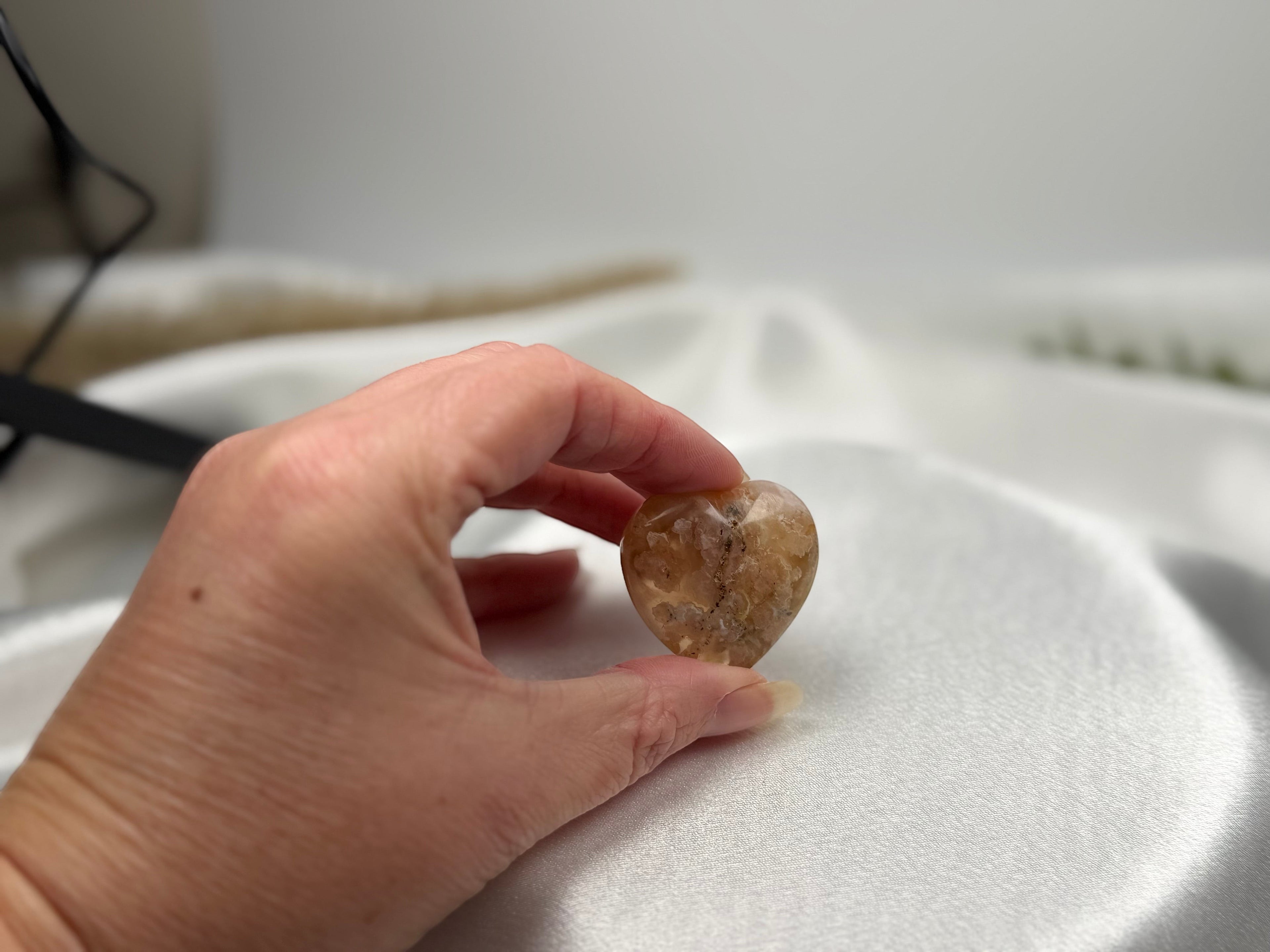 Treasured Energies polished flower agate crystal heart held in hand against a soft white satin background