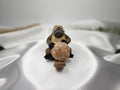 Treasured Energies flower agate crystal heart held by a small platypus figurine on a white satin background.