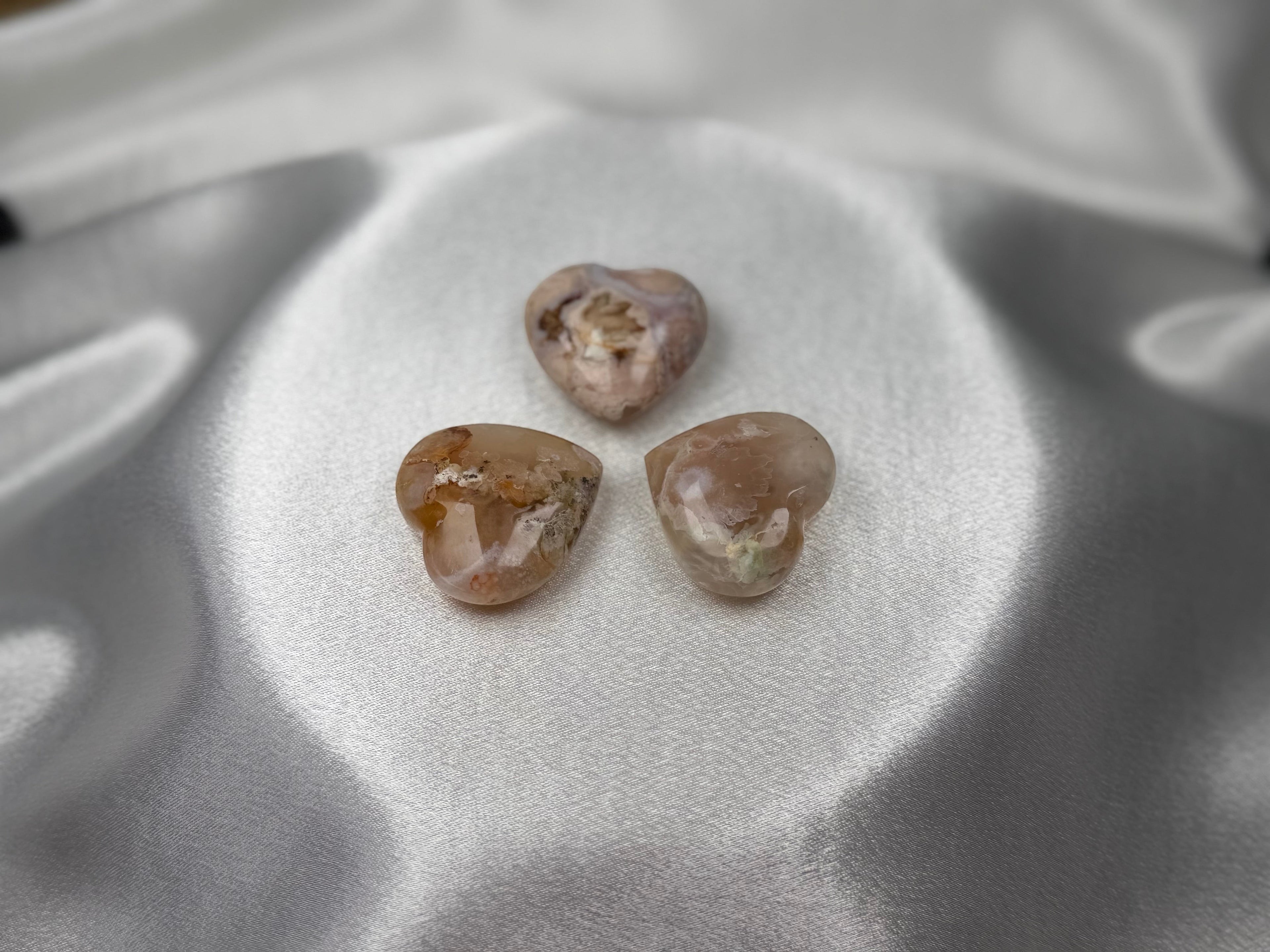 Treasured Energies polished flower agate crystal hearts with floral inclusions on a soft white satin background