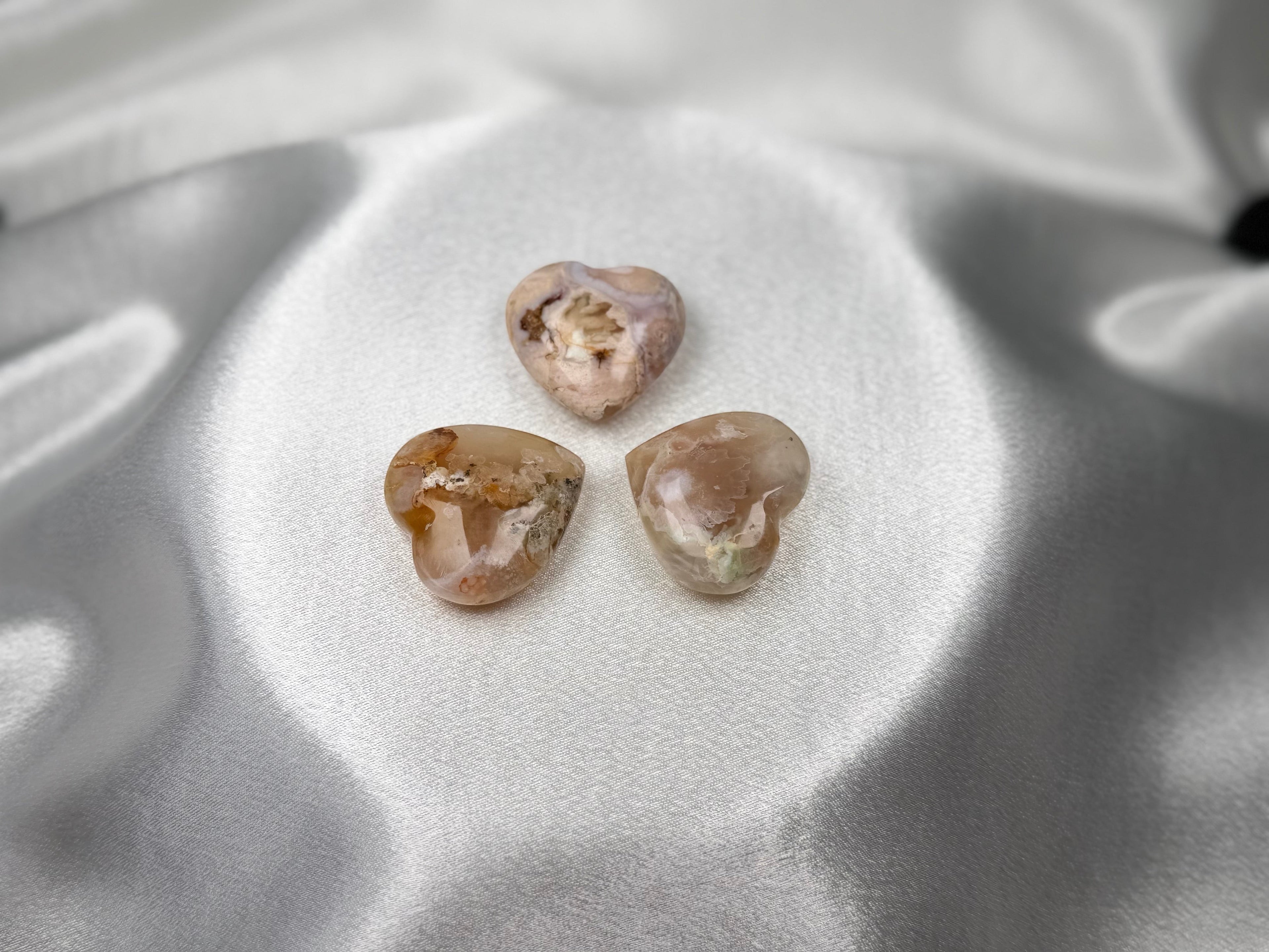 Treasured Energies flower agate crystal hearts with floral inclusions on a soft white satin background.