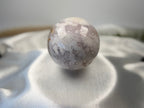 Treasured Energies flower agate sphere with druzy inclusions resting on a soft white satin fabric