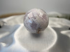 Treasured Energies polished flower agate crystal sphere with druzy inclusions resting on a soft white satin fabric.