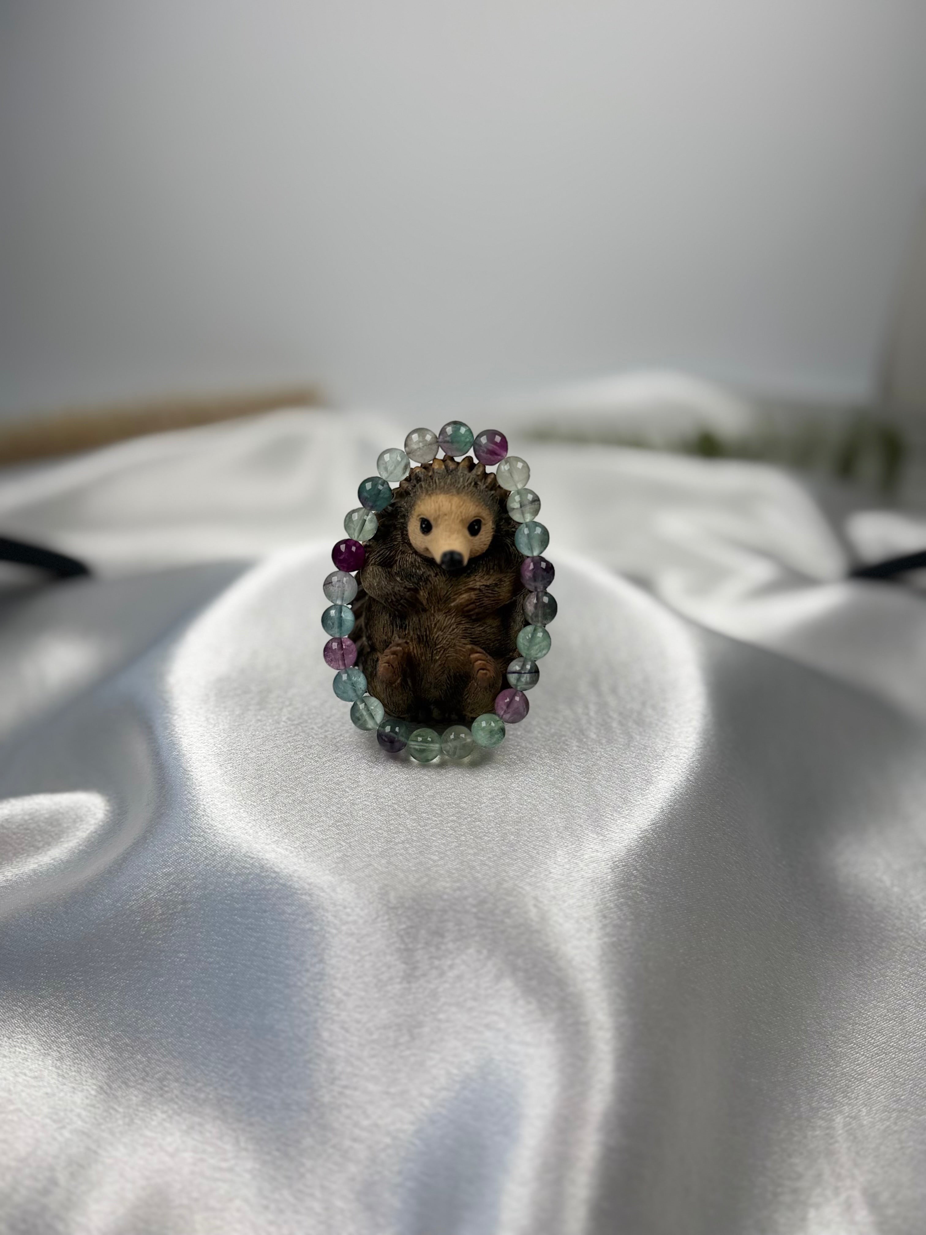 Treasured Energies fluorite gemstone beaded stretch bracelet encircling a small decorative hedgehog figurine