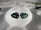 Treasured Energies polished fluorite crystal hearts in purple and green hues resting on a smooth white satin fabric.